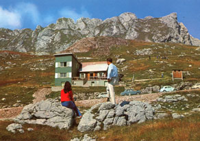 Obisk Zgornjega Posočja je bil pogosto povezan s hribolazenjem. Nekateri so se do gorskih vrhov dejansko povzpeli, drugi so jih raje občudovali z nižje ležečih in lažje dostopnih mest kot je na primer planinska koča na sedlu pod Mangartom, do katere pelje vozna cesta. (Arhiv Tolminskega muzeja)